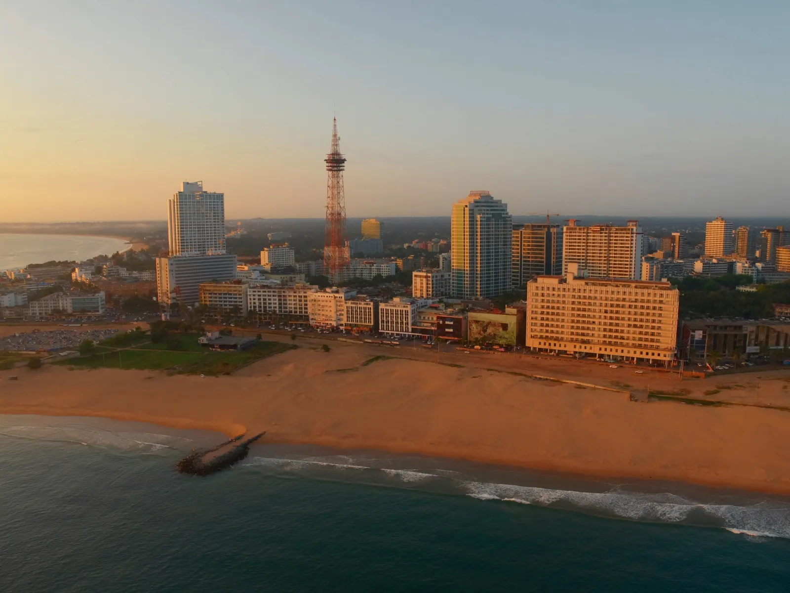 Colombo, Sri Lanka skyline at dusk with a modern telecommunications tower and office buildings along the Indian Ocean coastline, warm light, wide angle
