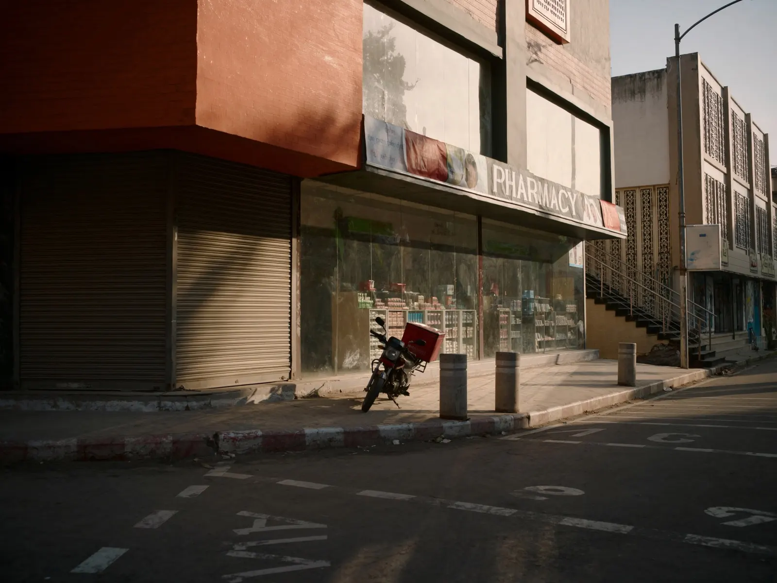 Indian city street in the morning with a modern pharmacy storefront and a parked delivery motorbike, warm light, documentary style, wide angle