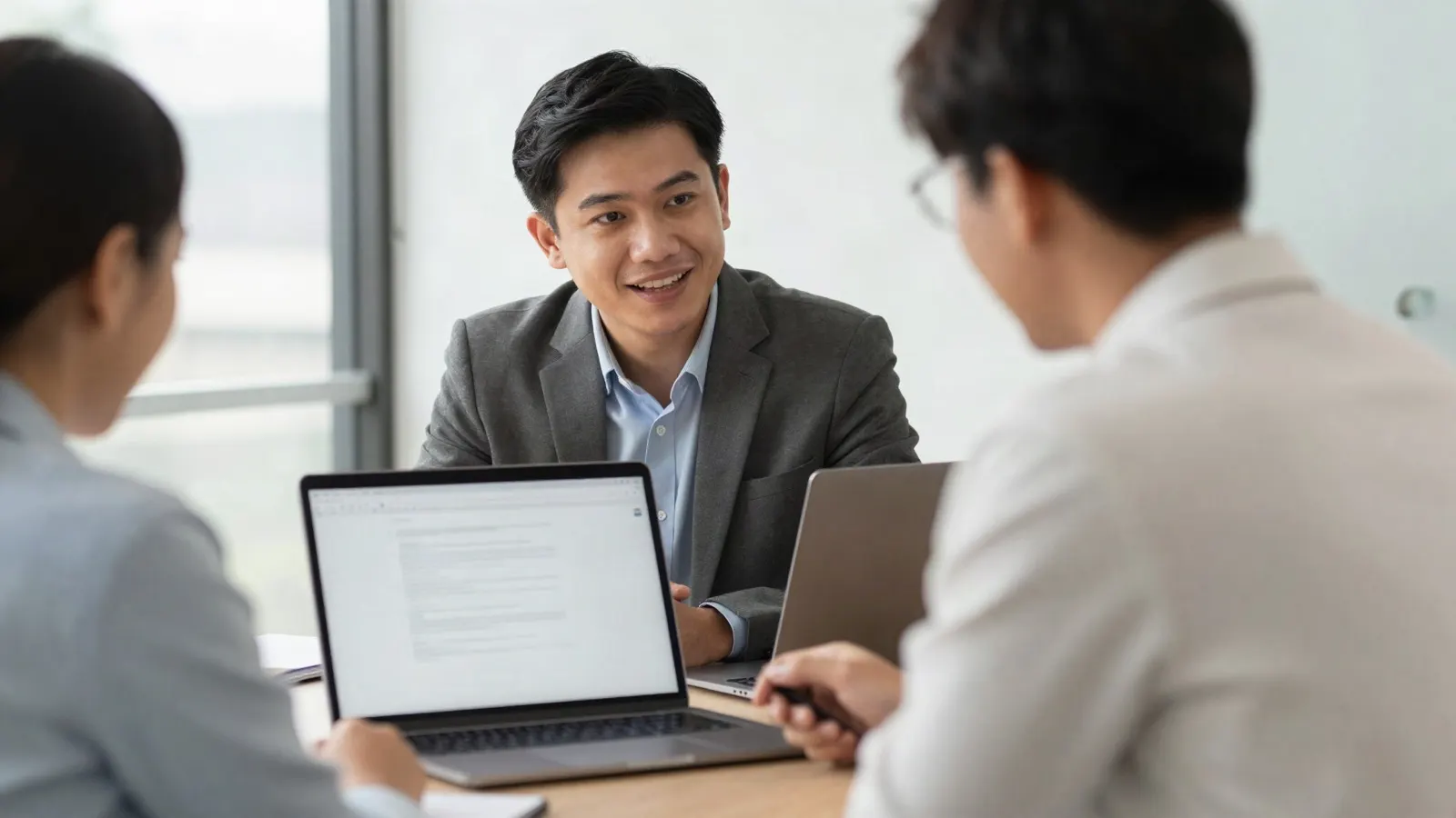 a Filipino manager and an employee in a bright corporate office having a performance review conversation over a laptop, warm daylight