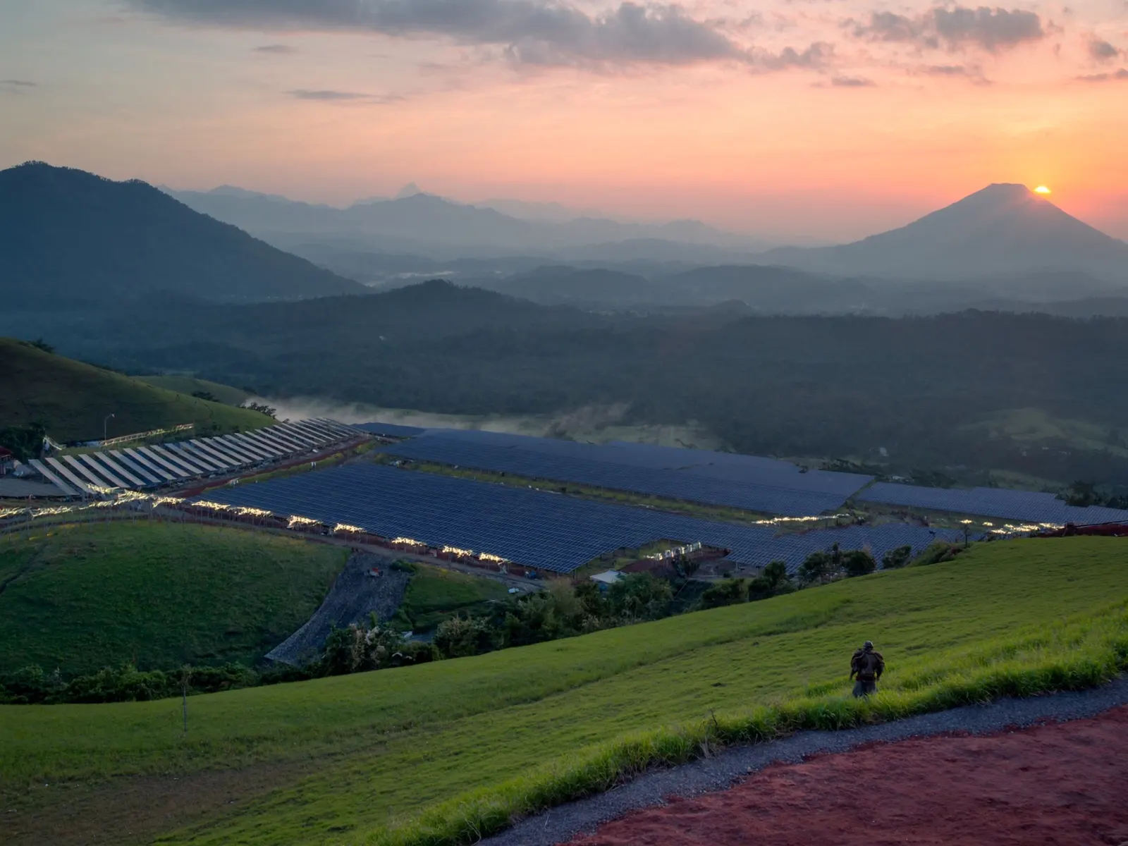 solar farm in Indonesia at sunrise with rows of panels on green hills and distant volcanoes, wide angle
