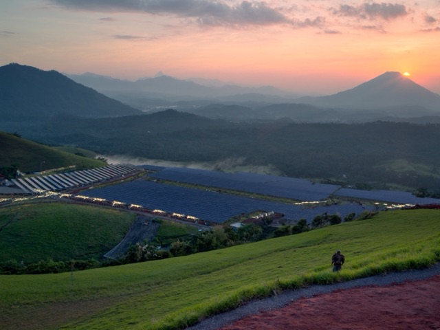 solar farm in Indonesia at sunrise with rows of panels on green hills and distant volcanoes, wide angle